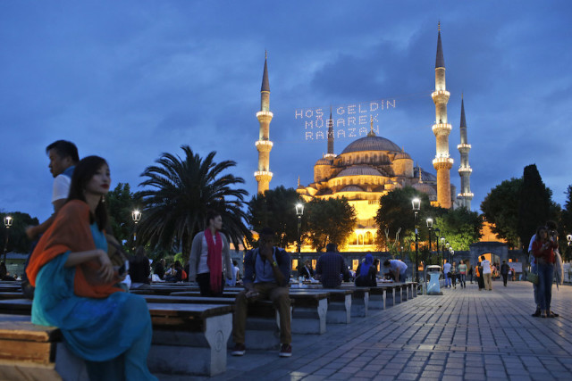 People gather backdroped by the the iconic Sultan Ahmed Mosque, better known as the Blue Mosque, decorated with lights marking the month of Ramadan, in the historic Sultanahmet district of Istanbul, Turkey, Thursday, June 18, 2015. The lights read in Turkish: 'Welcome Holy Ramadan'.  Muslims throughout the world are marking Ramadan - a month of fasting during which the observants abstain from food, drink and other pleasures from sunrise to sunset. After an obligatory sunset prayer, a large feast known as 'iftar' is shared with family and friends. (AP Photo/Emrah Gurel)
