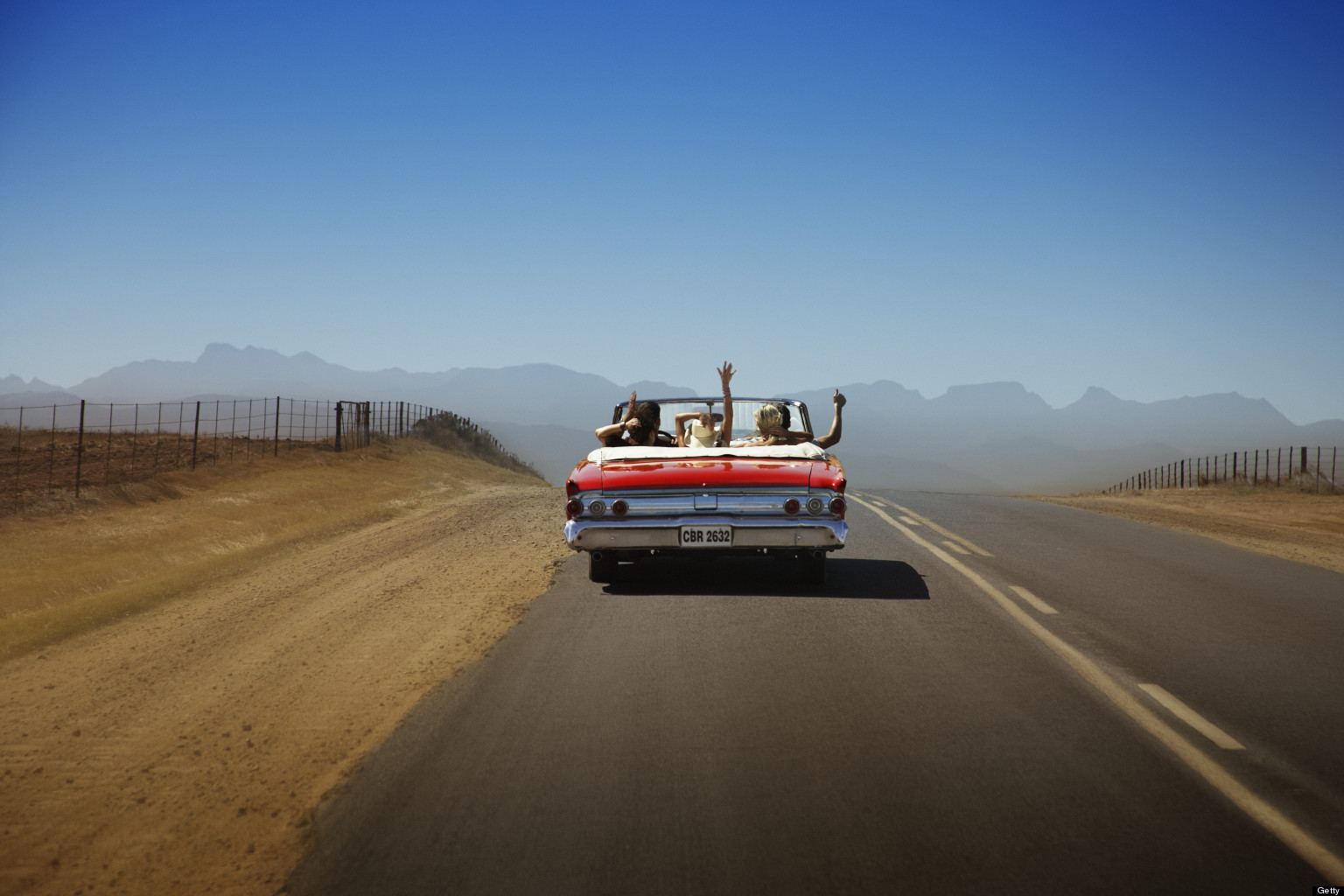 Five friends in convertible car, waving arms in air, rear view